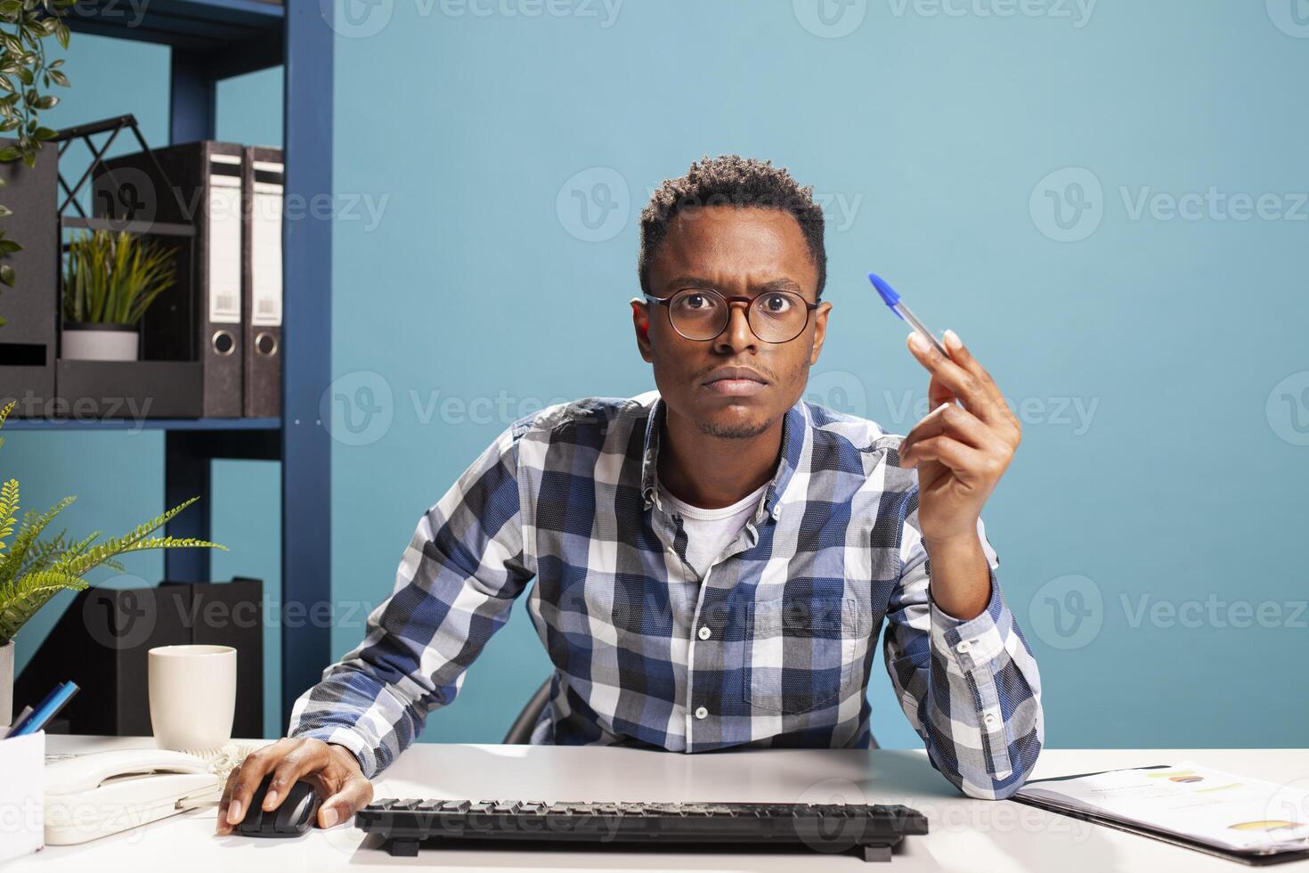 Company advisor with pen in hand, looking confused as he closely reviews business expenses on his computer monitor. Black entrepreneur seated in doubt and suspicion at office desk, analyzing data. photo