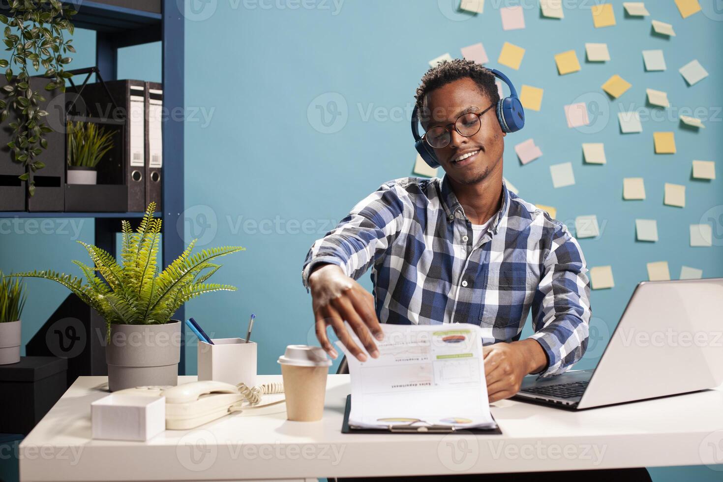 Calm male accountant listening to music and going over company documentation. Business advisor wearing headphones and flipping through papers on clipboard, reviewing financial data in marketing firm. photo
