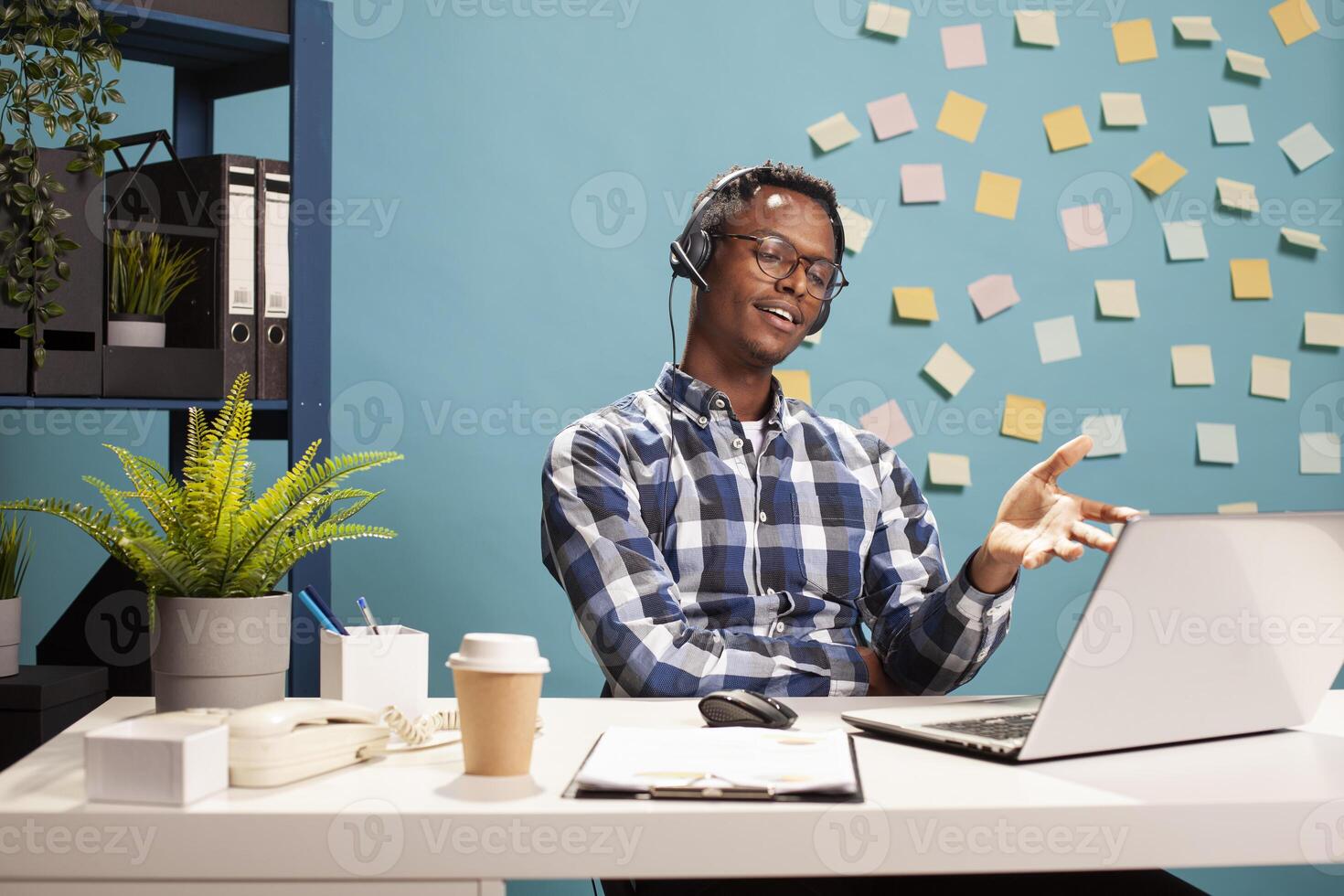 Company consultant at his office desk, providing phone support to a client regarding application paperwork. Male entrepreneur using his laptop to process information and on a call through his headset. photo