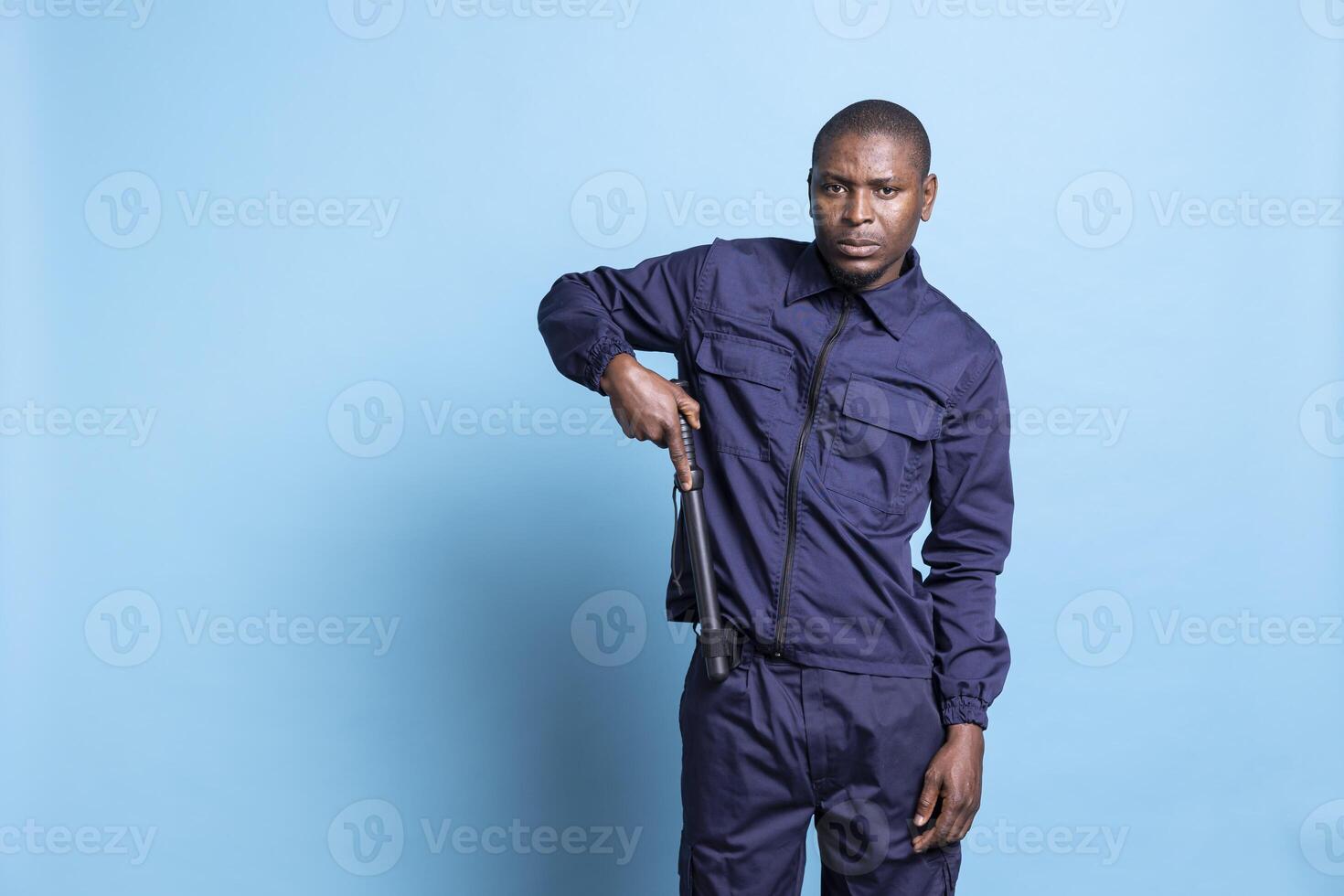 Security agent on duty taking out his baton against blue background, preparing for an attack or fight. Armed bodyguard in uniform holding his weapon getting ready for emergency defense. photo
