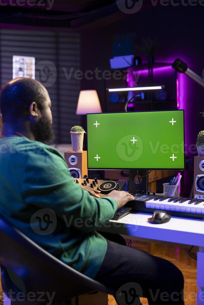 Audio engineer producing new music on display with greenscreen, working on mixing and mastering tracks in his home studio. Skilled artist having fun editing tunes on stereo console. photo