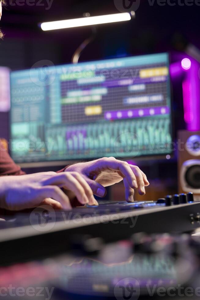 Sound engineer working with soundboard and midi controller to create the perfect tunes for his songs, recording and editing audio. Music composer adjusts volume levels during mixing sessions. photo