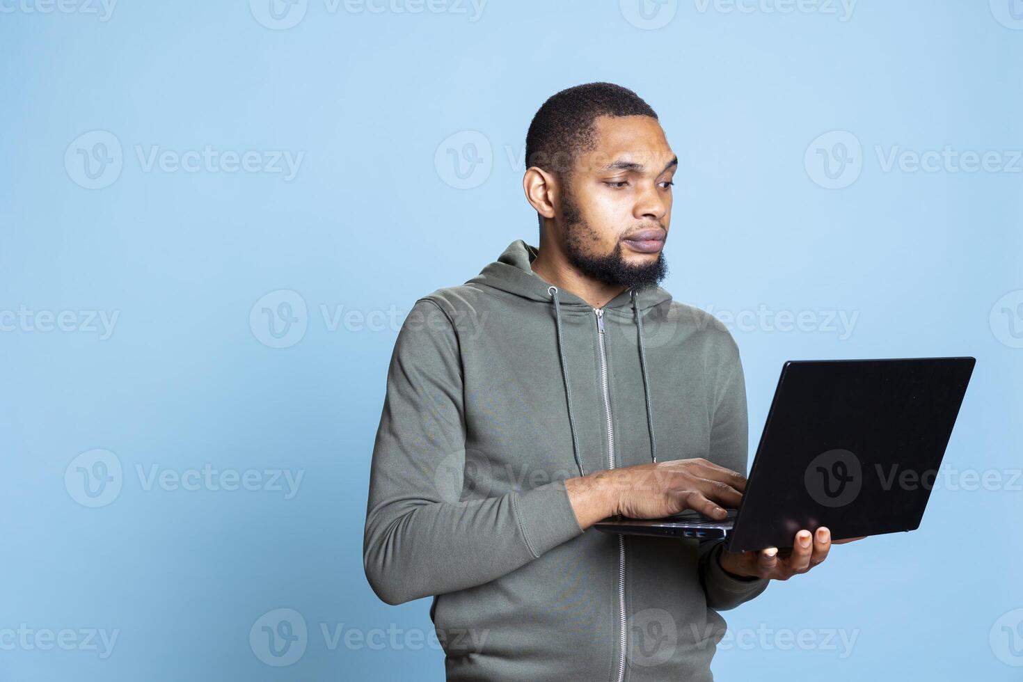 African american person smiling and carefree working on laptop, focused skilled man typing information and browsing online websites. Young adult does paperwork and writes emails. photo