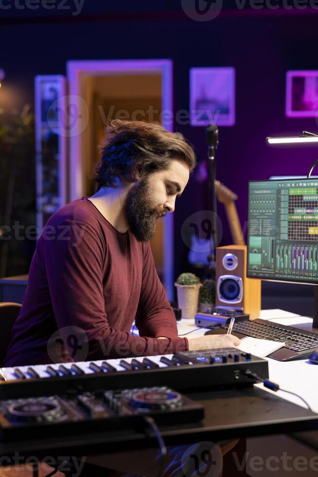 Young composer writing rhymes and lyrics to create new song in home studio, thinking about harmonic notes and lines to make cool music. Audio engineer producing soundtracks with gear. photo