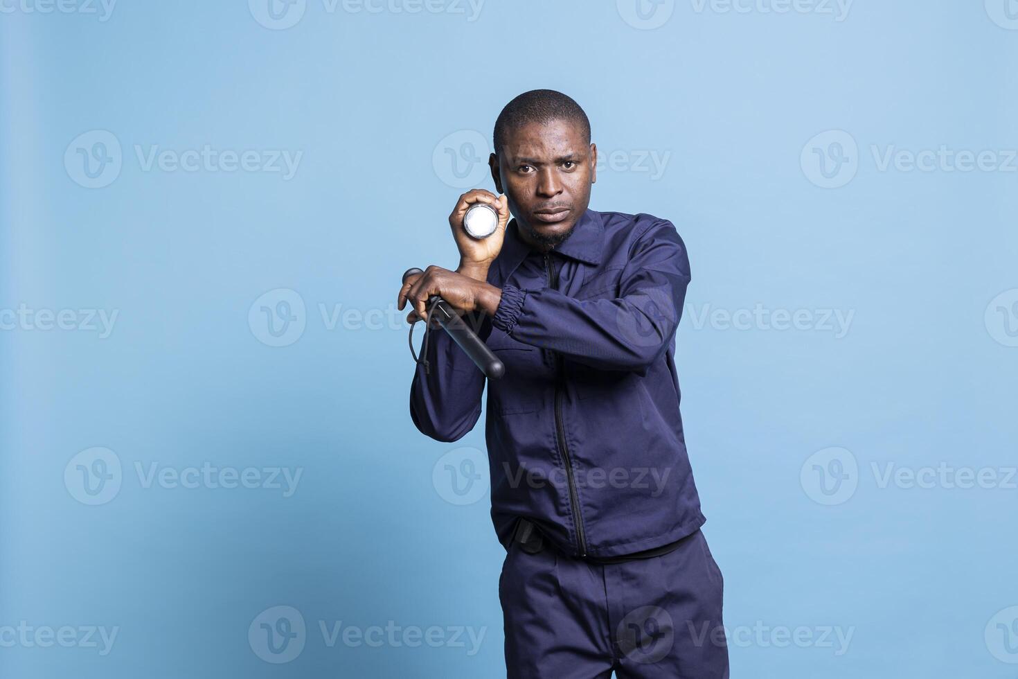 African american bodyguard patrolling the perimeter in the dark, lighting the way with a flashlight against blue background. Security agent inspecting the premises with a lantern. photo