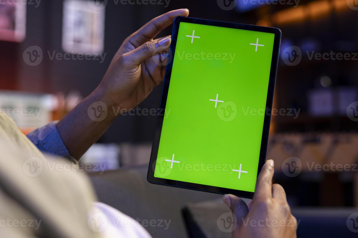 Young remote worker uses green screen on a tablet at his house, feeling carefree in the living room and solving his freelancing tasks. Male person being casual in his apartment, teleworking. photo