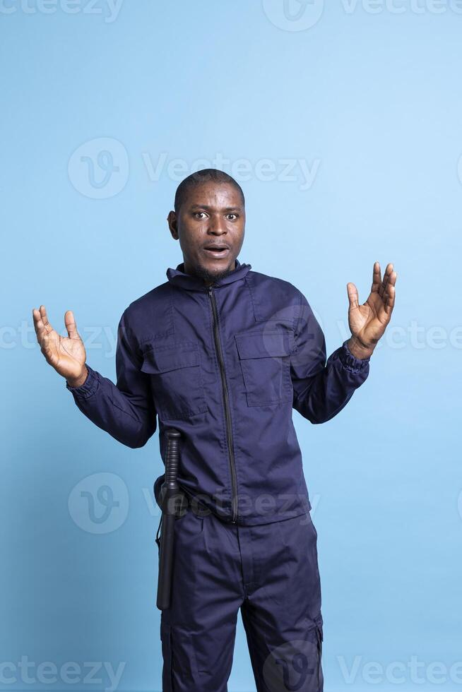 African american officer with uniform acting surprised on camera, having a shocked reaction after seeing something surprising. Male security agent acting amazed against blue background. photo