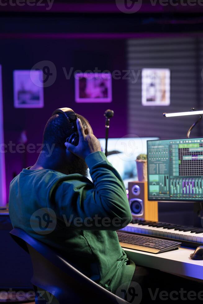 Musician playing piano keys and editing to improve the sound quality of audio recordings in his home studio, putting on headset. Music producer uses midi controller to manipulate sounds. photo
