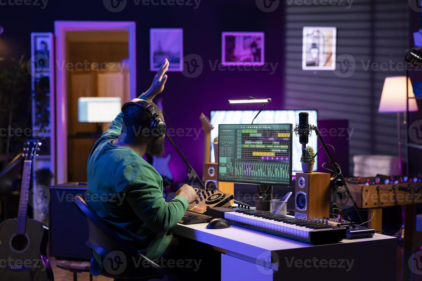 Confident music composer mixing sounds on digital audio software, creating a cool atmosphere in his home studio. Young cheerful producer composing new soundtracks with stereo gear. photo