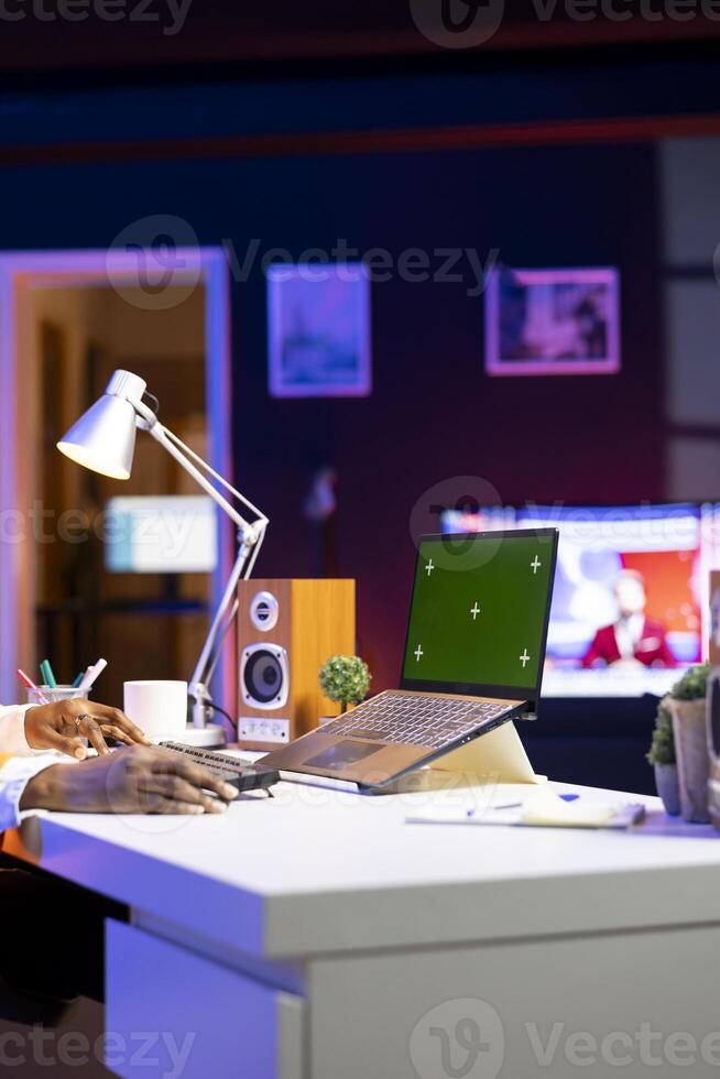 Person at home office desk using green screen mockup laptop, composing social media posts. Remote content creator employee monitoring engagement on chroma key isolated screen notebook photo
