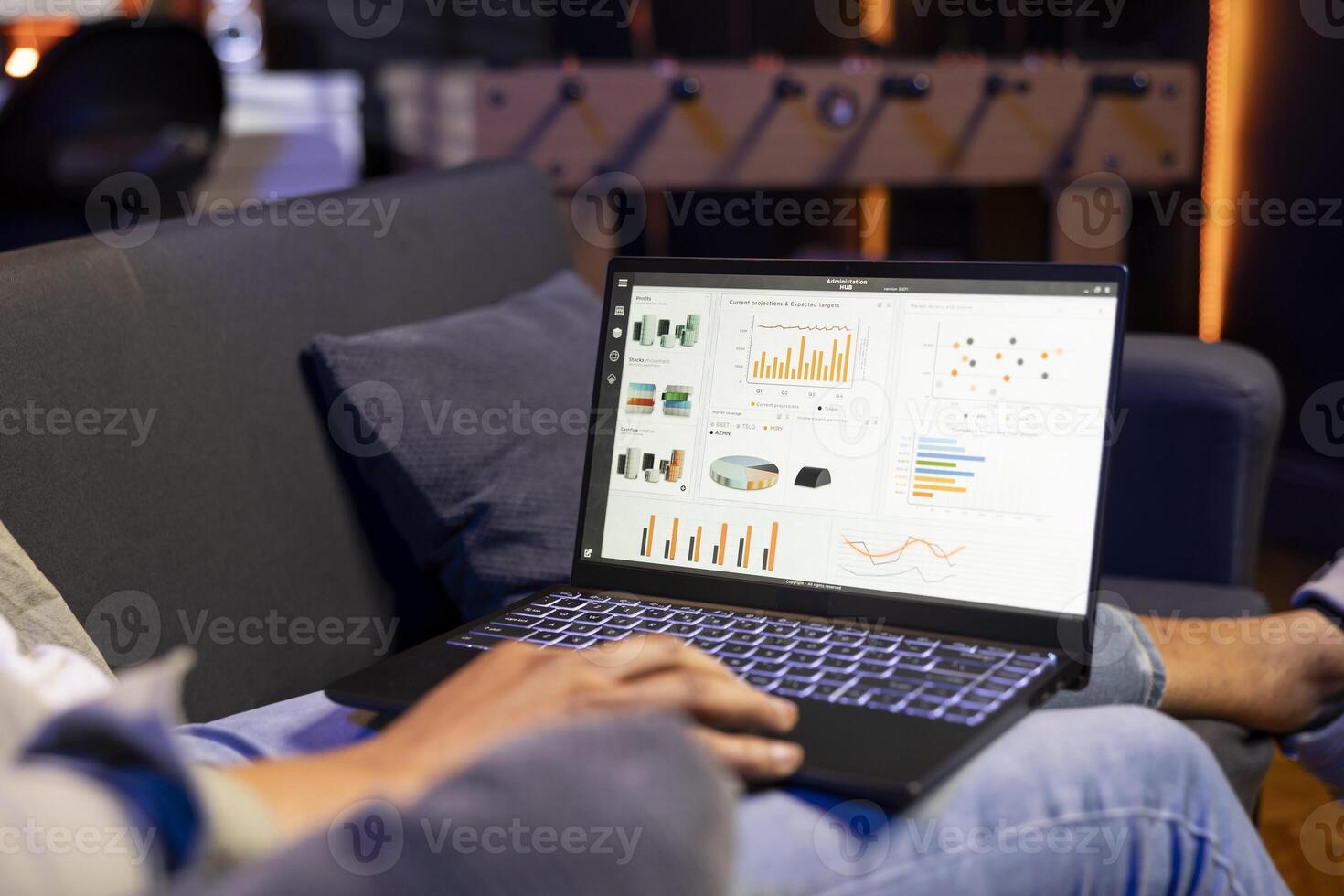 African american guy studying analytics and archived data for a project, reviewing infographics and relaxing on his sofa. Young adult working remotely from the comfort of his home. photo