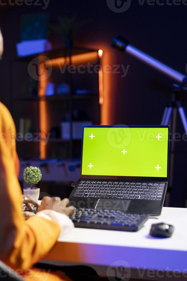 Teleworker in home office editing documents on mockup laptop, updating reports and files, typing text. Freelancer managing digital paperwork within file directories on green screen notebook photo