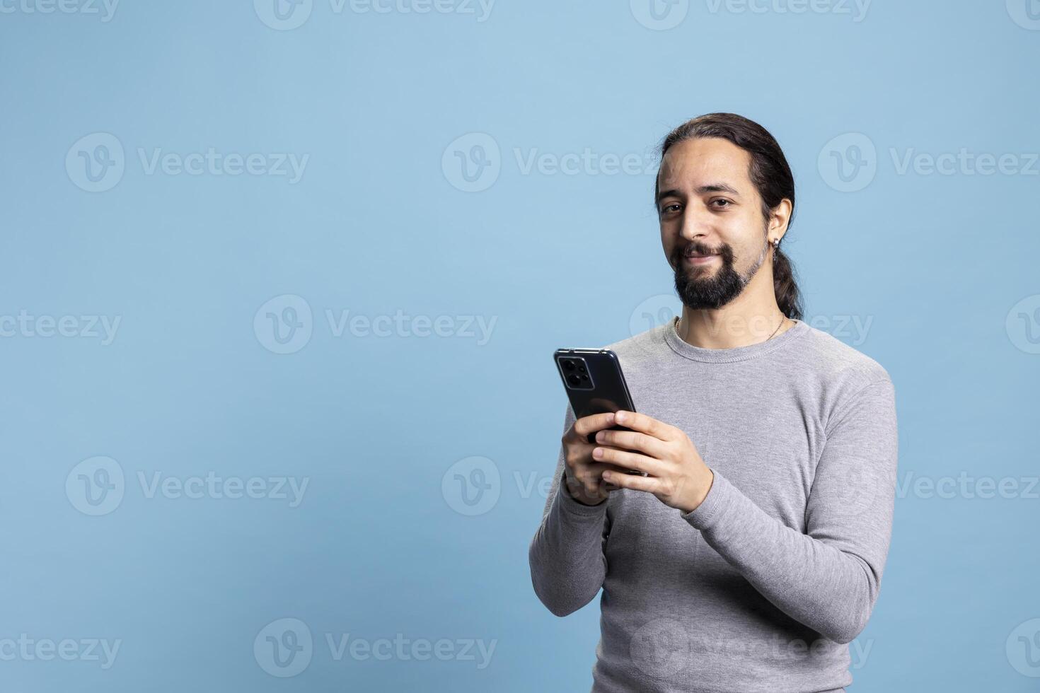 Professional young man in casual clothes using a phone with a pensive expression, embodying the modern digital professionalism. Cool male model uses device on blue background. photo