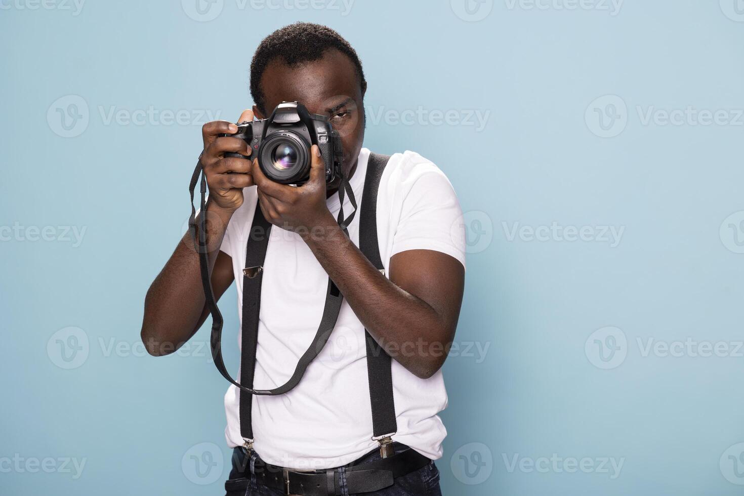 Confident male photographer in a white t shirt and suspenders grasping his camera, demonstrating his passion for photography. The studio setting enhances his professional and stylish appearance. photo