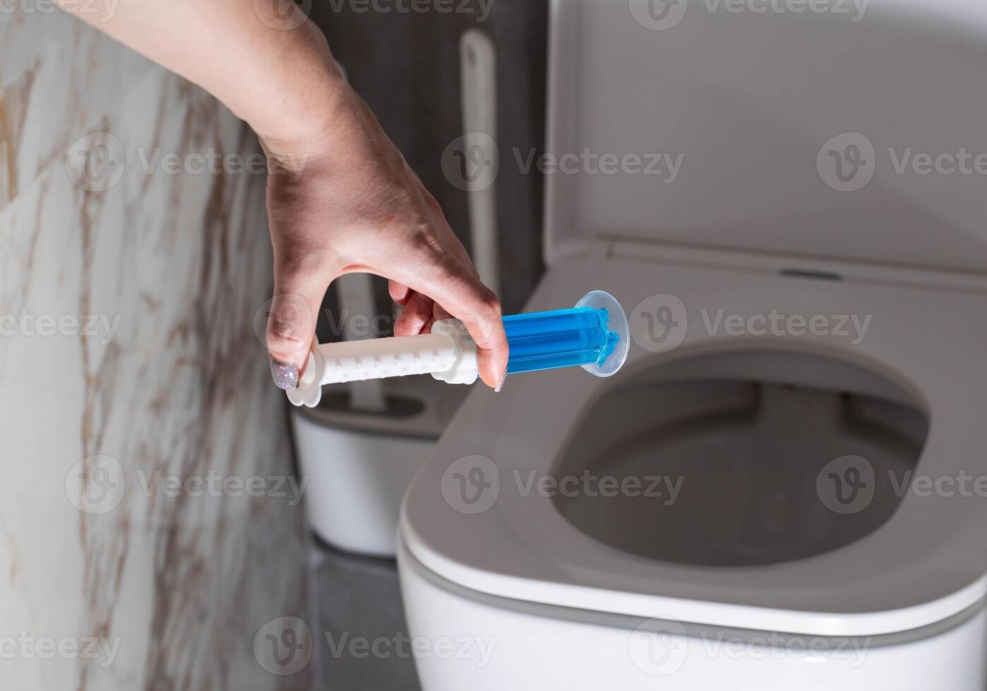 A syringe with a gel for cleaning and disinfecting the toilet bowl in a hand against the background of a toilet. Antibacterial effect photo