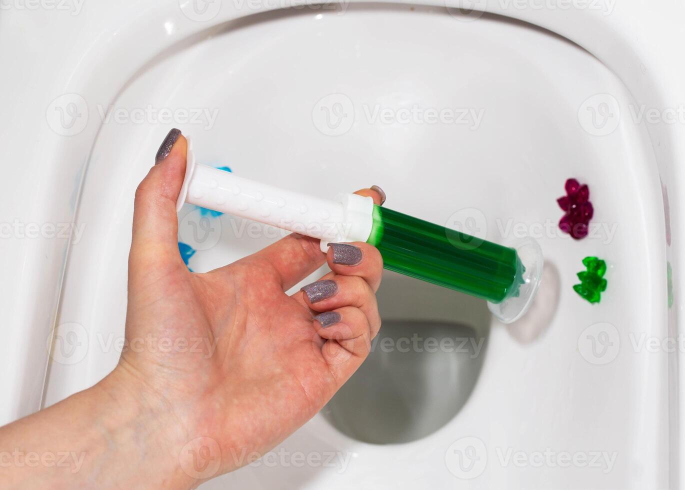 Green gel in a syringe in a hand against the background of a toilet. Toilet cleaning and disinfection, antibacterial effect, close-up photo