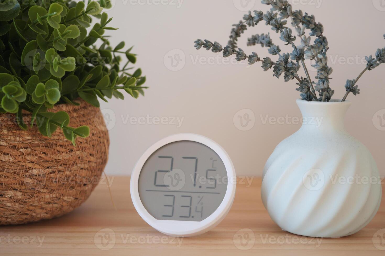 Indoor temperature and humidity display with plants on wooden table photo