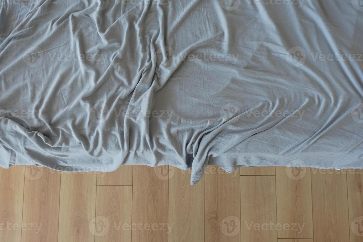Messy bed with wrinkled gray sheets in a cozy room photo
