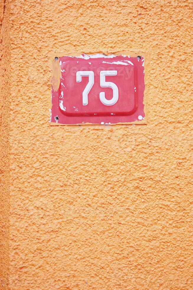 Numeric house number 75 displayed on vibrant orange wall photo