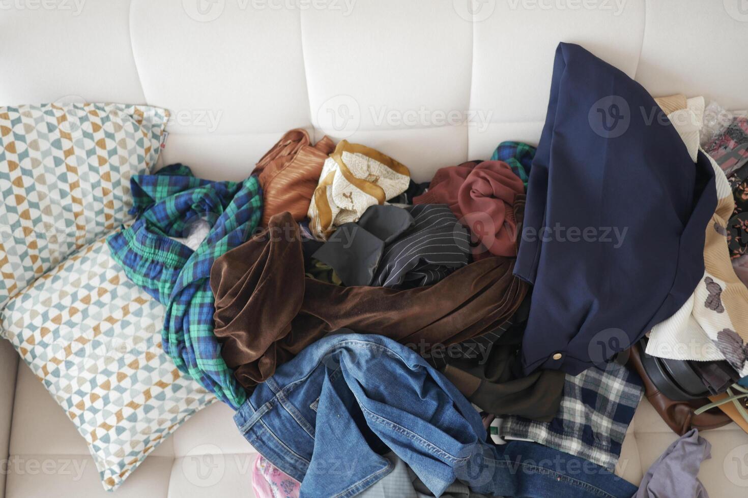 Pile of assorted clothes on a white couch in a cozy living room photo
