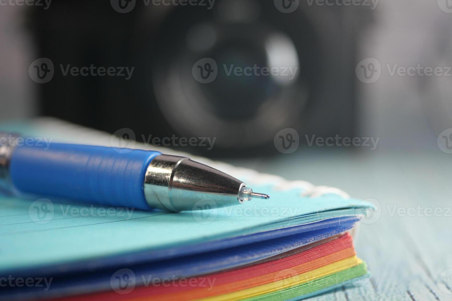Colorful notebook and pen on a wooden surface with a camera backdrop photo