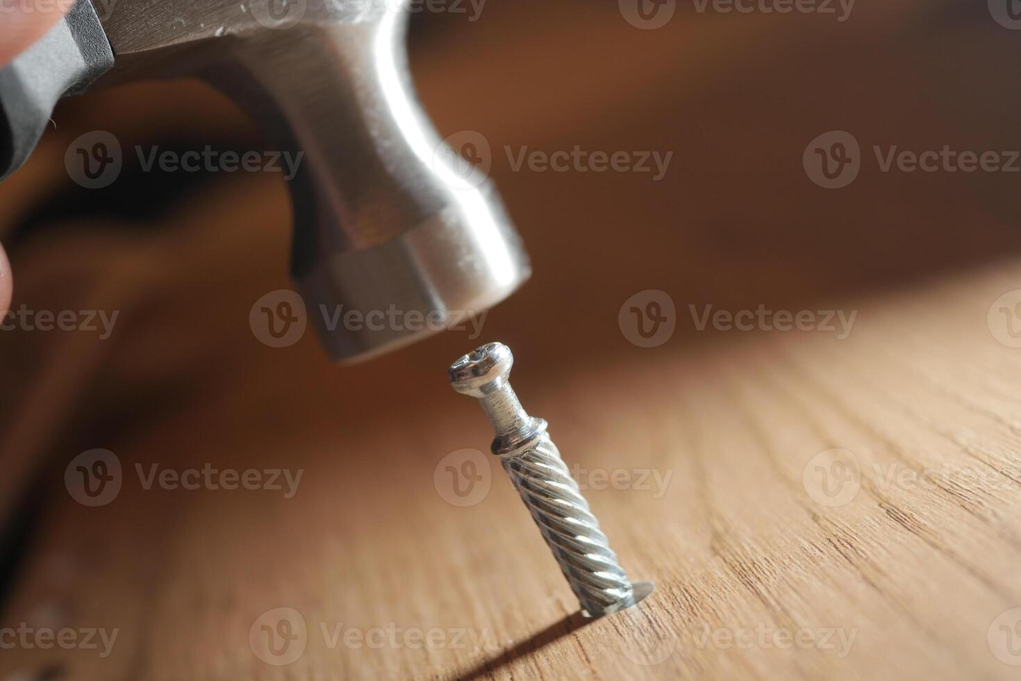 Hammer strikes a screw on a wooden surface during assembly photo