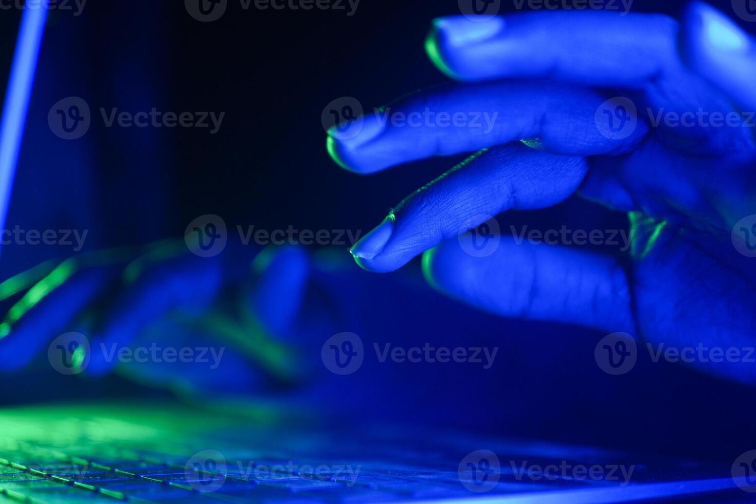 hacker Hands typing on a laptop illuminated by blue and green light photo