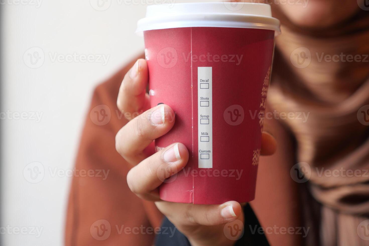 Warm drink in a red paper cup held by a person indoors photo