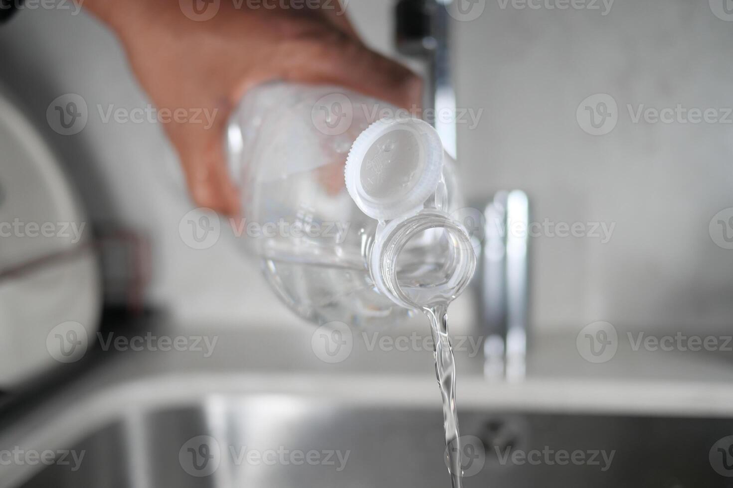 Pouring clear water from a plastic bottle into a kitchen sink photo