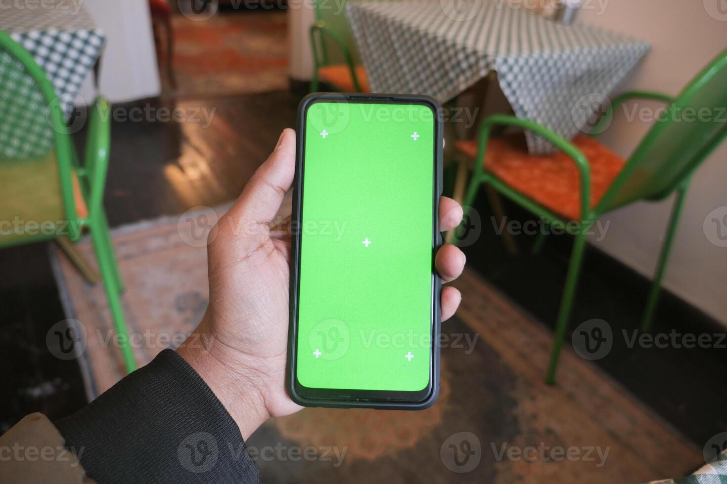 Hand holding smartphone with green screen in cozy cafe setting photo