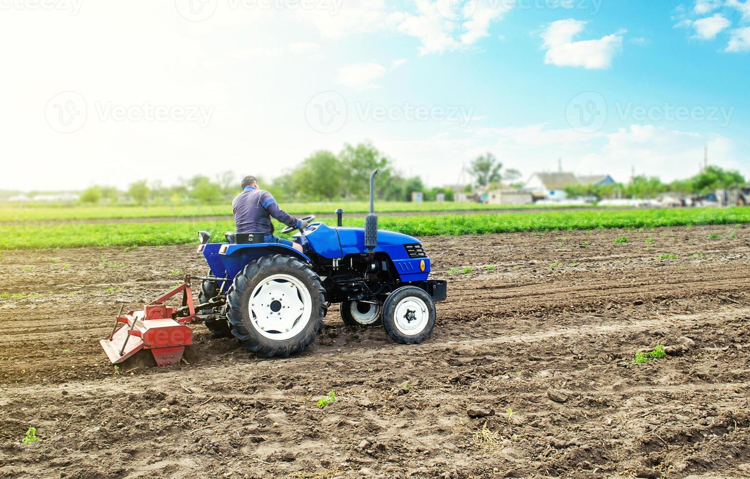 Farmer on a tractor with milling machine loosens, grinds and mixes soil. Field preparation for new crop planting. Loosening surface, cultivating the land for further planting. Farming and agriculture. photo