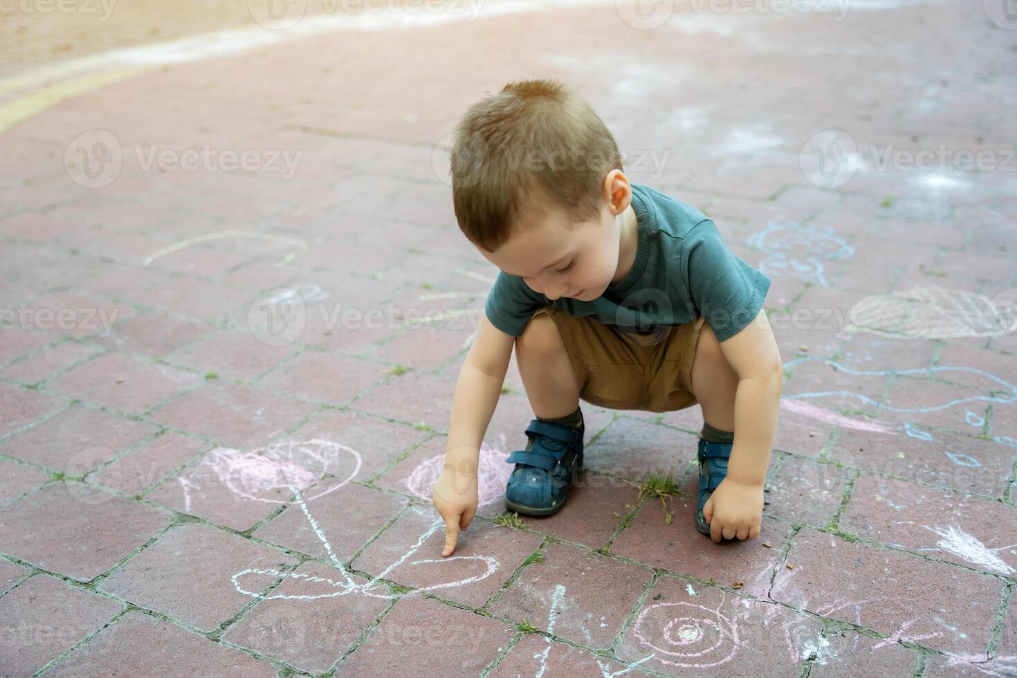 Little toddler boy two or three years old points his finger at children's drawings drawn in chalk. Playtime for children. Children's games. Selective focus photo
