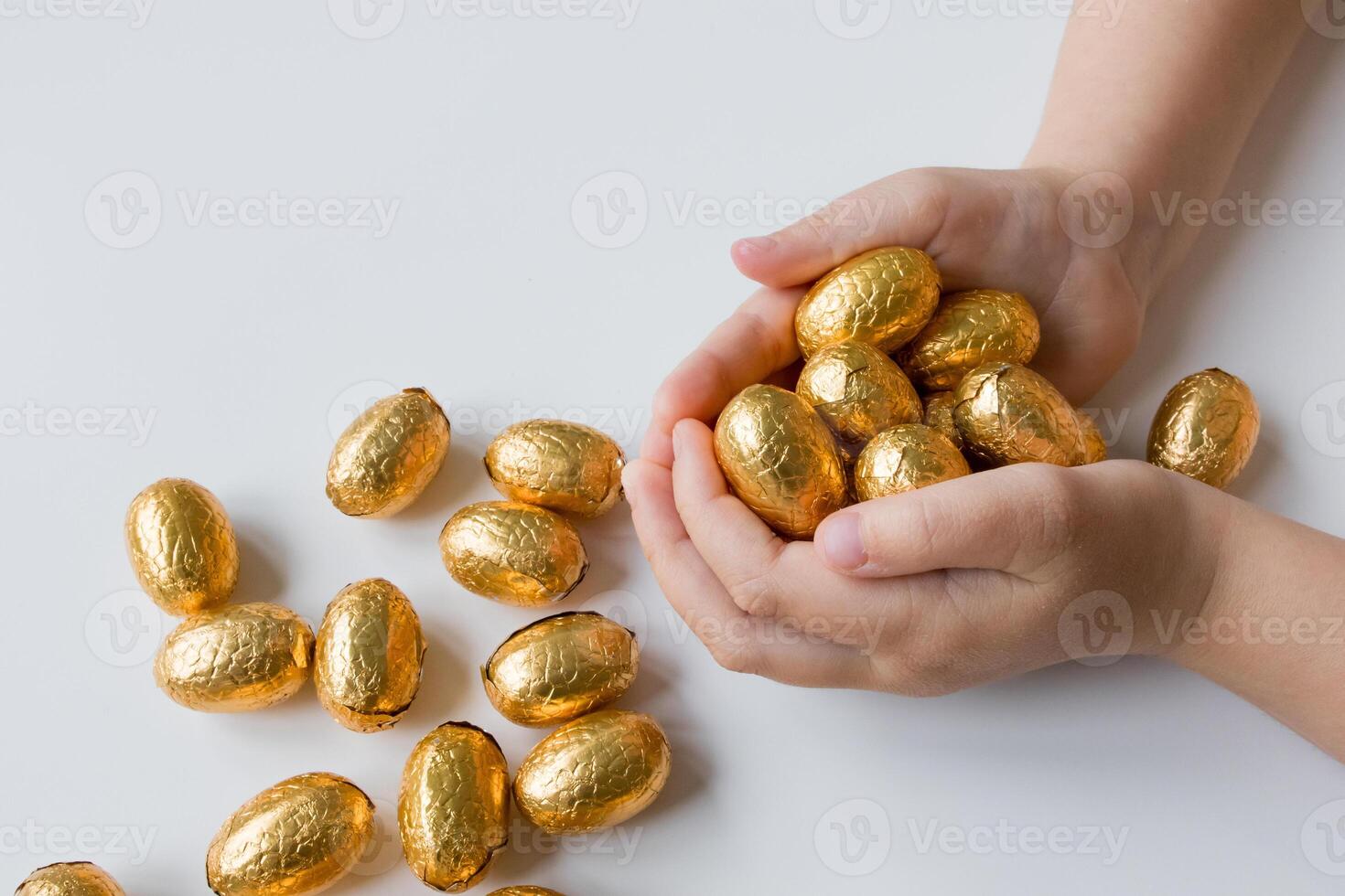 Child holding handful of golden wrapped chocolate eggs on white background photo