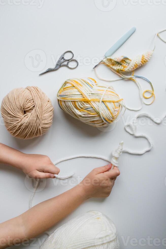 Child crafting with yarn and tools on white surface photo