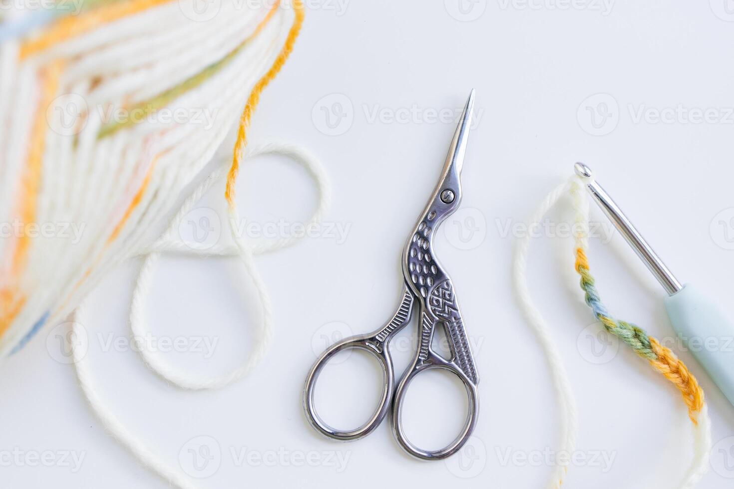Crochet tools and yarn ball with bird shaped scissors on white surface photo