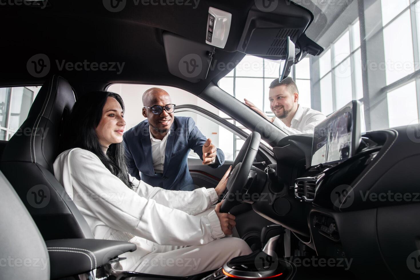 Happy caucasian woman is sitting in the drivers seat of a grey sedan. New car from a dealership representative. The concept of test drive, buying an electric car or renting photo