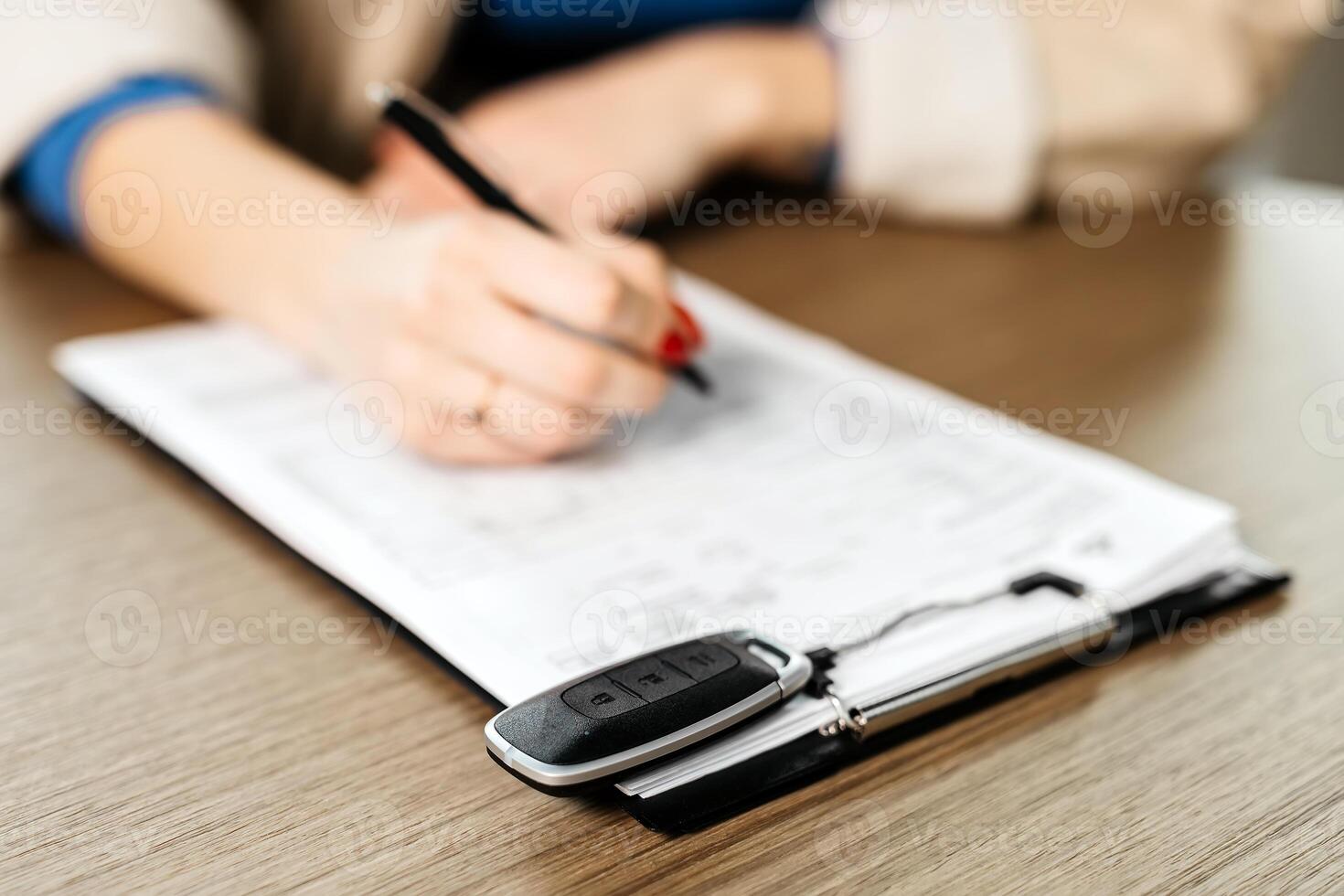 Female signing car insurance document or lease paper. Writing signature on contract or agreement. Buying or selling new or used vehicle. Car keys on table photo