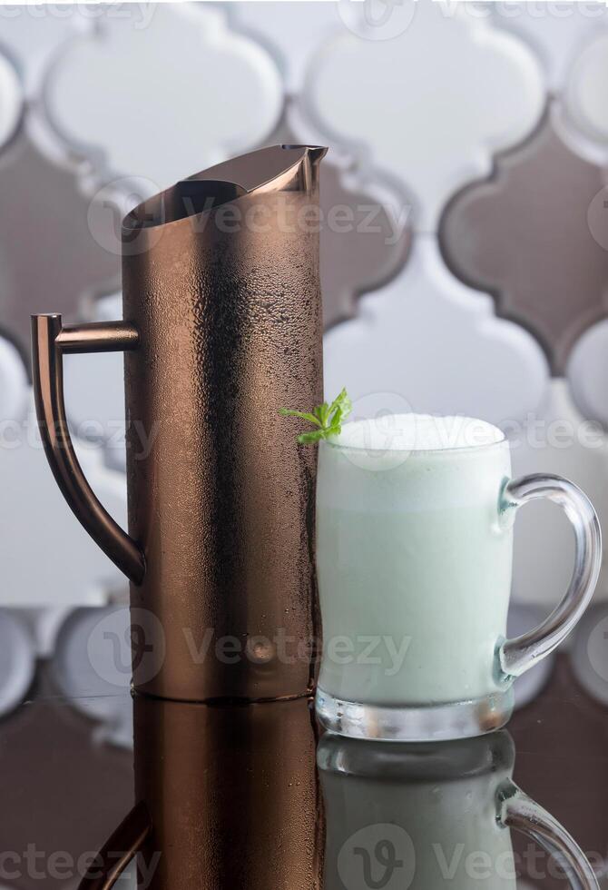 Laban Erbil a yogurt based drink served in a glass mug alongside a metal jug isolated on background side view of traditional Iraqi beverage photo