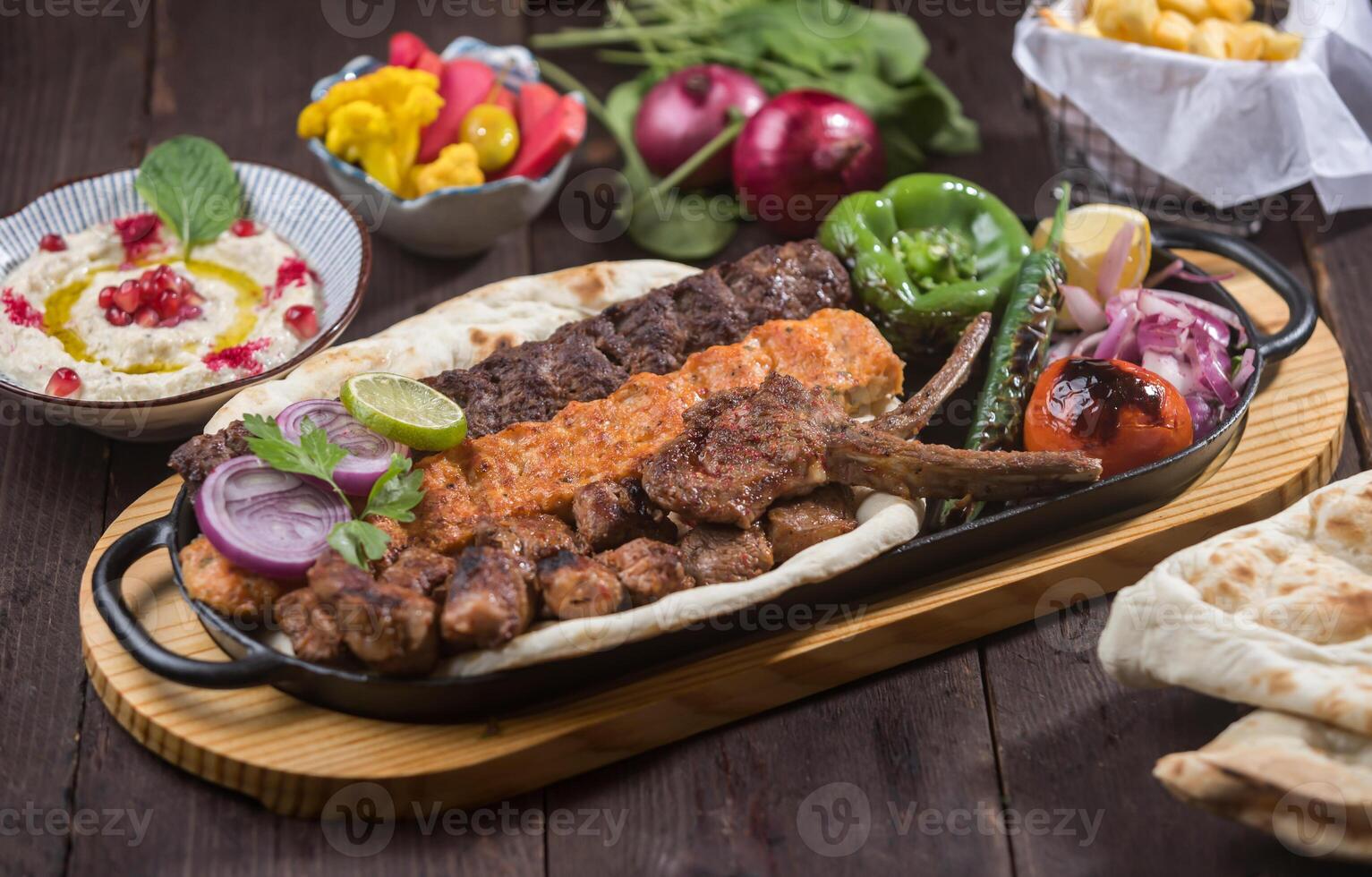Mixed Grill Platter served in tray with meat kebab, chicken kabab, tikka, boti, lamb chops, pita bread, hummus, and salad isolated on wooden table side view of Middle Eastern bbq photo