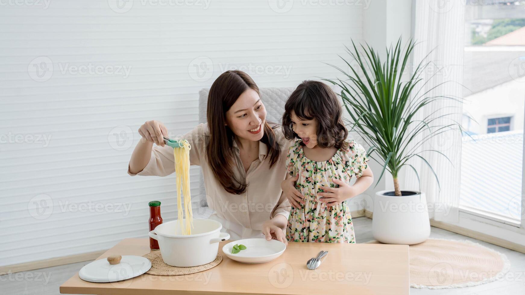 Joyful mother and daughter cooking pasta together in a bright modern kitchen, sharing a fun and loving bonding moment during mealtime preparation at home. photo