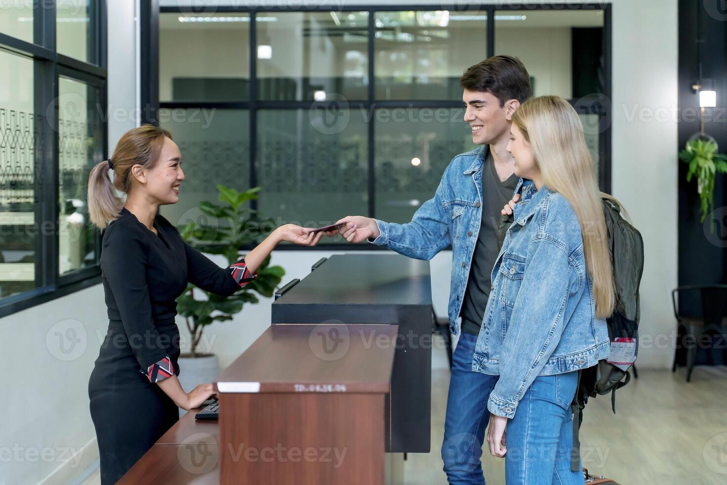 Young couple handing passport to hotel receptionist at front desk during check-in, showing hospitality, travel documentation, and customer service photo