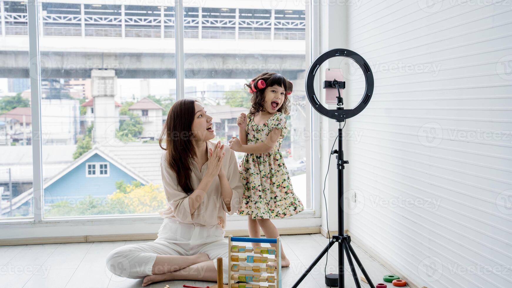 Joyful mom and daughter dancing and recording fun content at home with smartphone and ring light, spending quality time together in cozy living space. photo