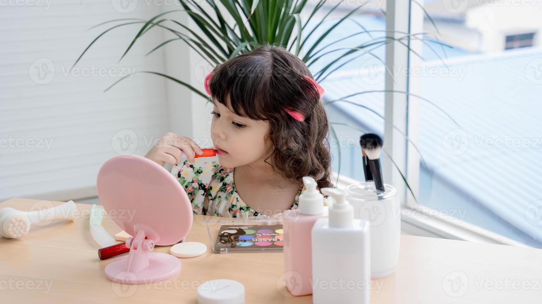 Adorable little girl playing with makeup in front of a mirror, applying lipstick with focus and curiosity, imitating adult beauty routines in a playful moment. photo