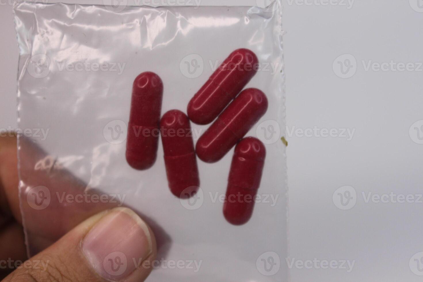 A person holding up four red pills in a plastic bag photo