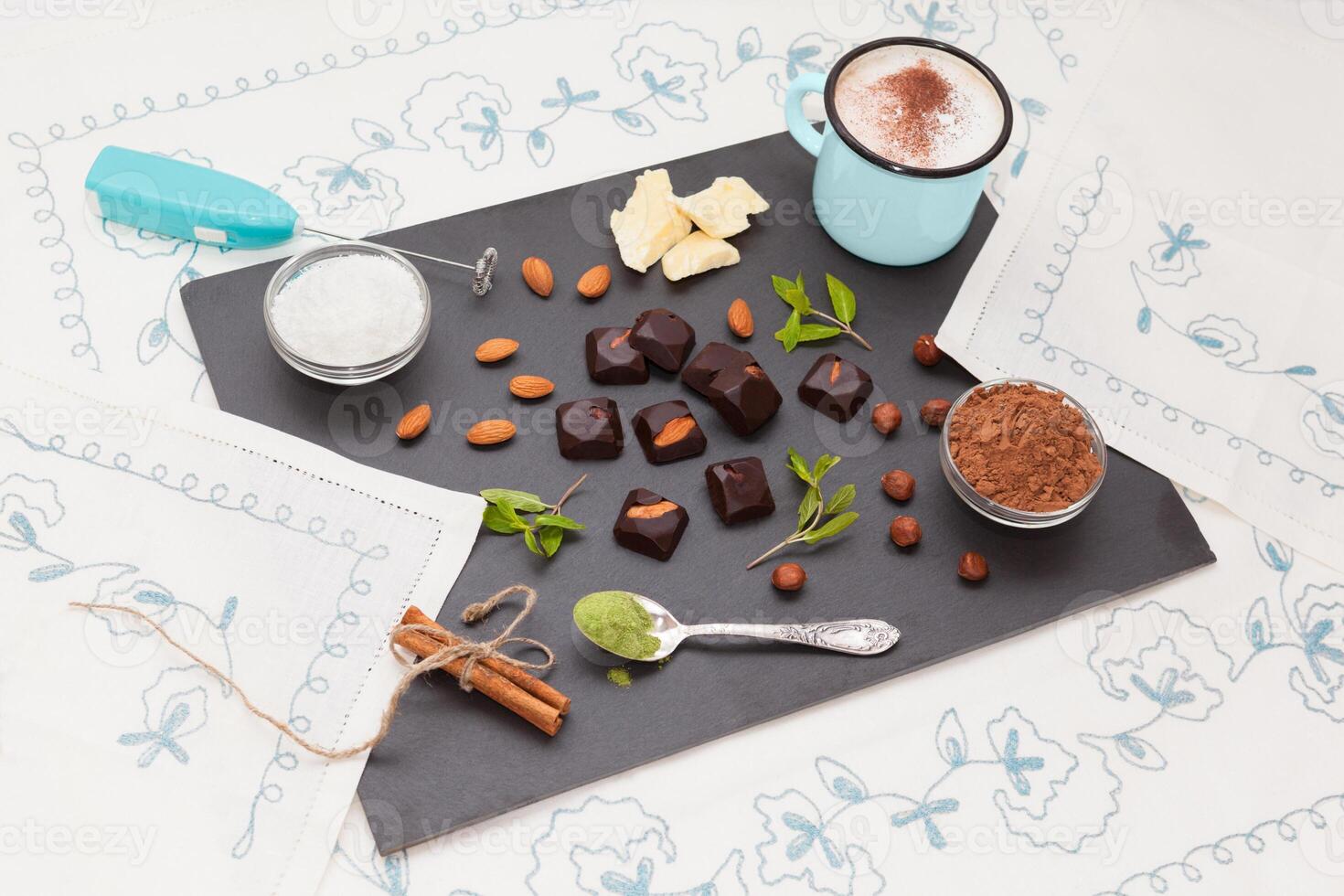 Homemade chocolates with almonds and hazelnuts, without shugar, no preservatives, alternative sweets with stevia, healthy dietary food, with blue cup of coconut milk cappuccino. Top perspective view. photo