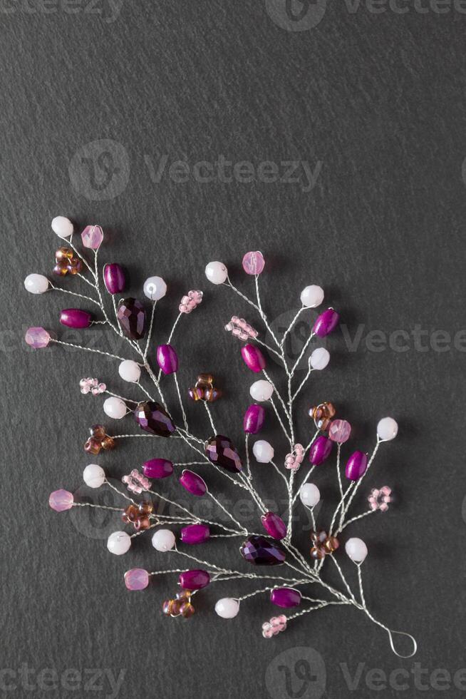 Beautiful handmade crafted embellishment, purple branch with beads and crystals, lying flat on the dark gray stone rectangular background, vertical top view photo