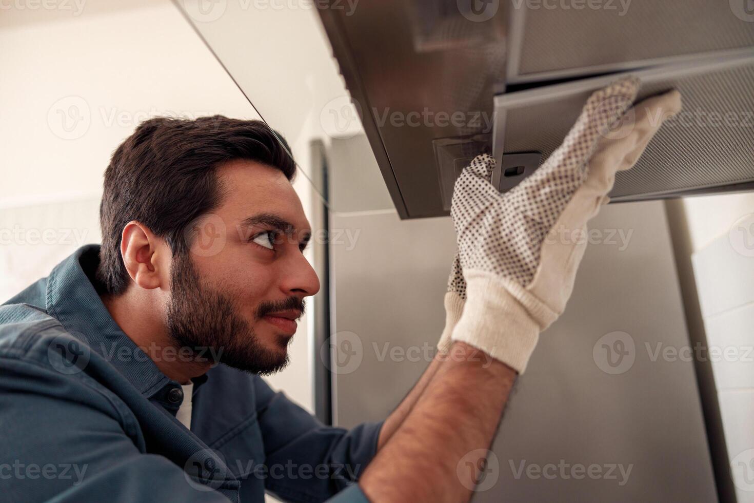 Handyman in uniform repairing kitchen extractor, replacing filter in cooker hood.Maintenance concept photo
