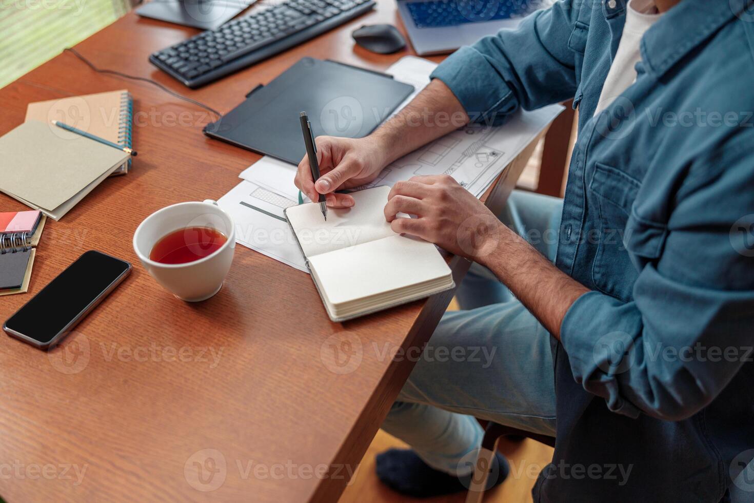 Close up of man hands making notes in notepad while sitting on his workplace photo