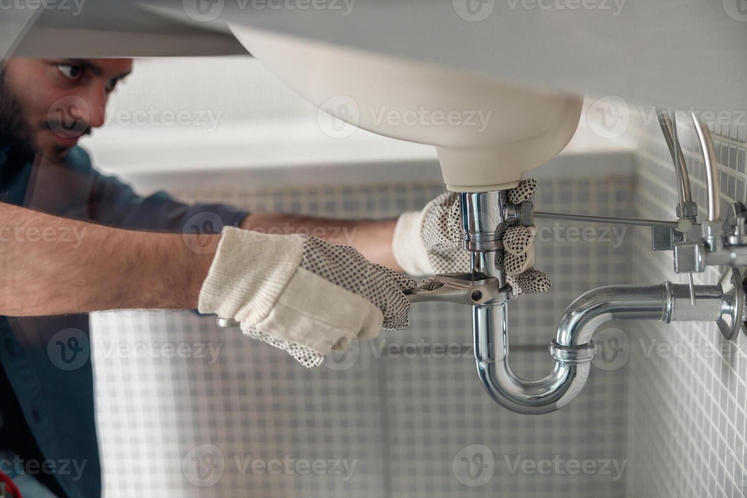 Close up of indian plumber is repairing faucet of a sink at bathroom using adjustable wrench photo