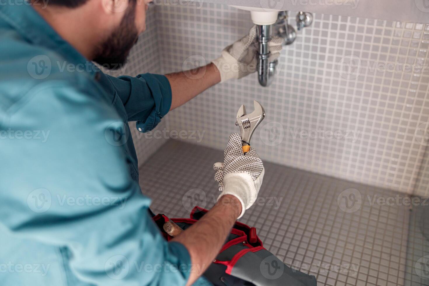 Close up of plumber is repairing faucet of a sink at bathroom using adjustable wrench photo